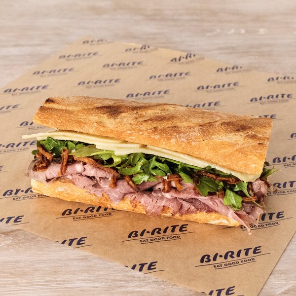 A sandwich on a Bi-Rite branded paper with visible layers of meat, lettuce, and cheese.