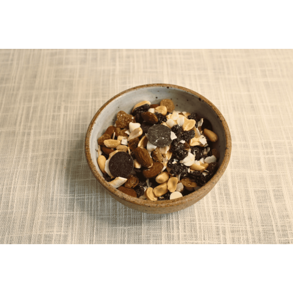 A bowl filled with a variety of nuts, seeds, and chocolate pieces on a textured surface.