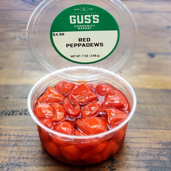 A clear plastic container labeled 'Red Peppadews' from Gus's Community Market, showing red pickled peppers.